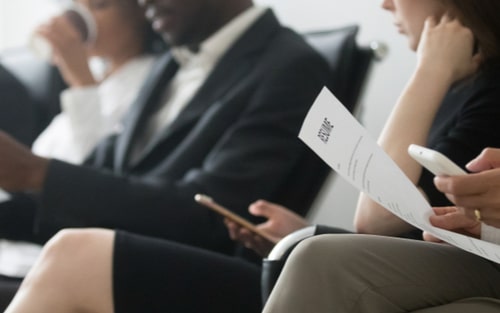 people waiting to go in for an interview holding their resumes