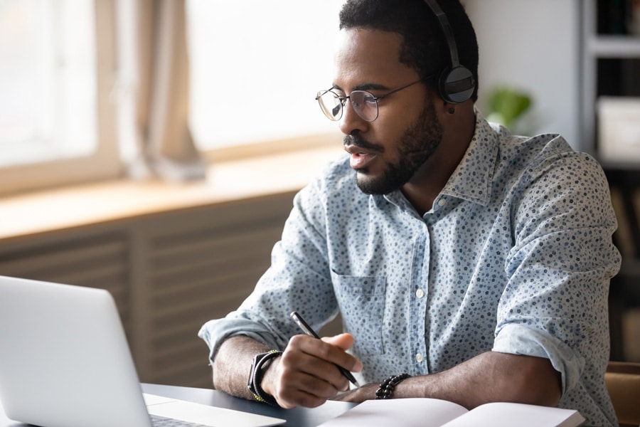 man with head set on holding a pen and staring into his computer