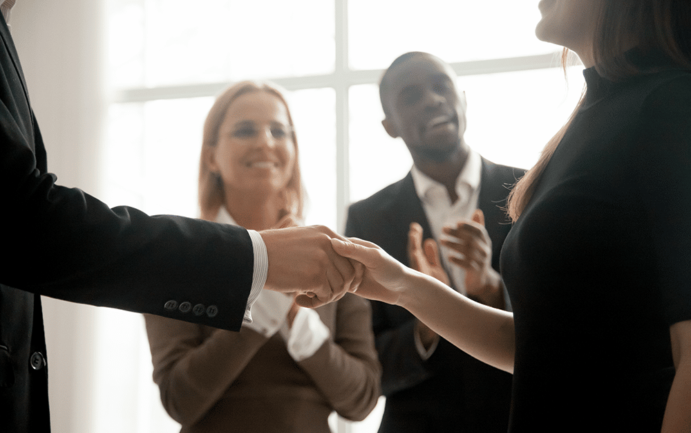 man and woman shaking hands at a meeting with people applauding in the background