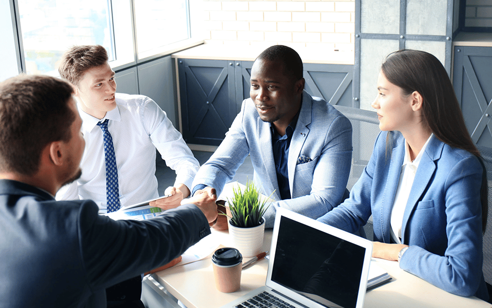 men shaking hands during a meeting with another man and woman present at the table